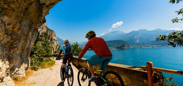 Cycling woman and man riding on bikes at sunrise mountains and Garda lake landscape. Couple cycling MTB enduro flow sentiero ponale trail track. Outdoor sport activity. &copy; Gorilla - stock.adobe.com
